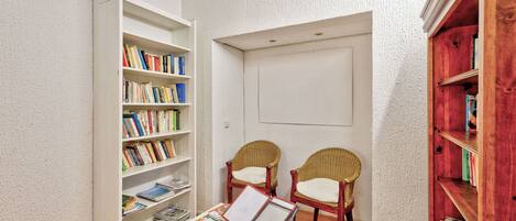 A reading area with a white bookshelf, two wicker chairs, a small table with magazines, and a red bookshelf.