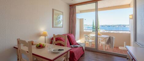 Een eetgedeelte met een tafel, stoelen en een kroonluchter. Er is een balkon met uitzicht op zee en gebouwen.