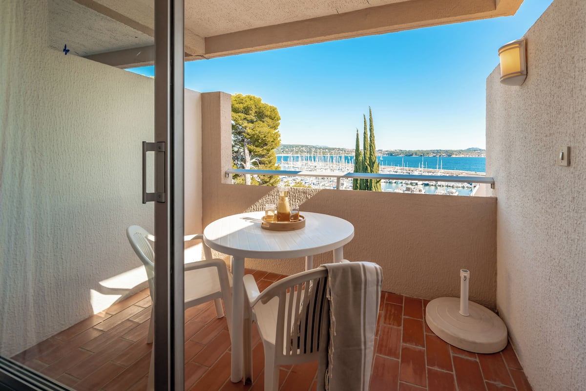 A balcony with a table and chairs, overlooking a marina and the sea.