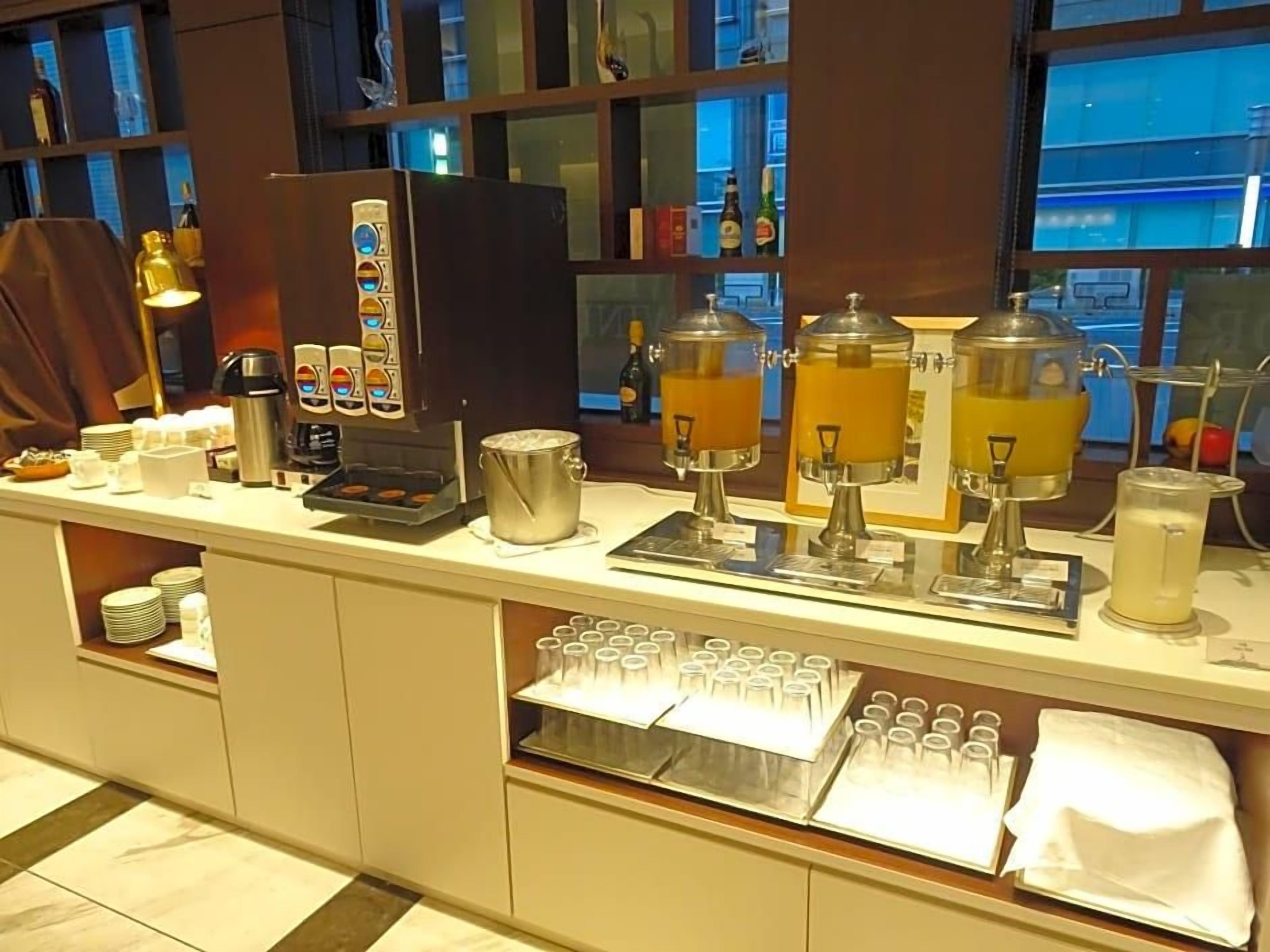 A buffet setup with coffee machines, a beverage dispenser, and a glass display case.
