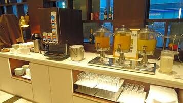 A buffet setup with coffee machines, a beverage dispenser, and a glass display case.