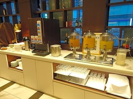 Montaje tipo bufé con máquinas de café, dispensador de bebidas y vitrina de vidrio.
