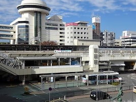 Un edificio moderno con una torre circular, un paseo peatonal cubierto y una parada de autobús.