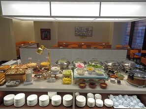 A buffet setup with various food items and utensils, a seating area with orange chairs, and a modern interior design. - Hotel Toyota Castle (Toyota)