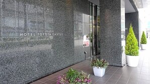 A modern hotel entrance with a dark stone facade, a glass door, and potted plants. - Hotel Toyota Castle (Toyota)