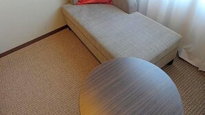 A small, single-occupancy room with a sofa bed, a round table, and a carpeted floor. - Hotel Toyota Castle (Toyota)