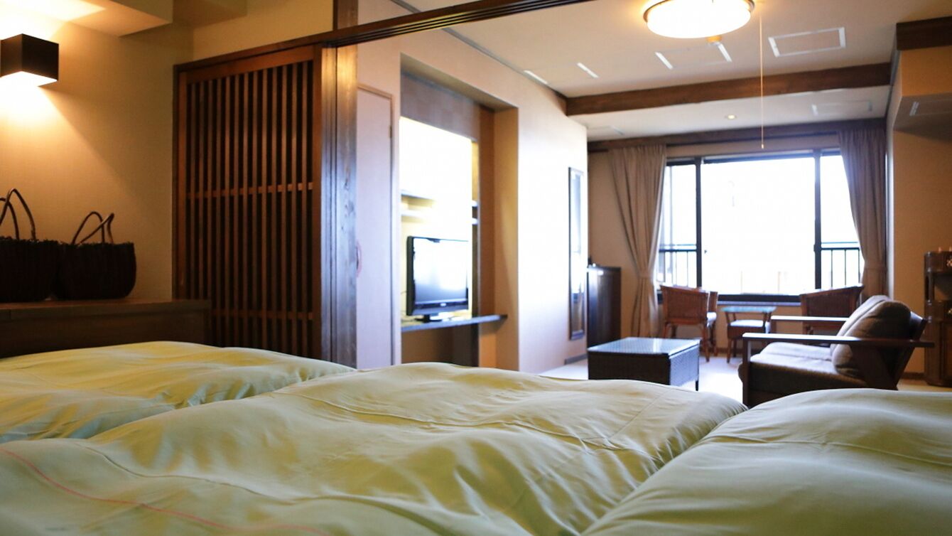 A hotel room with two beds, a desk, a chair, and a balcony with a view.