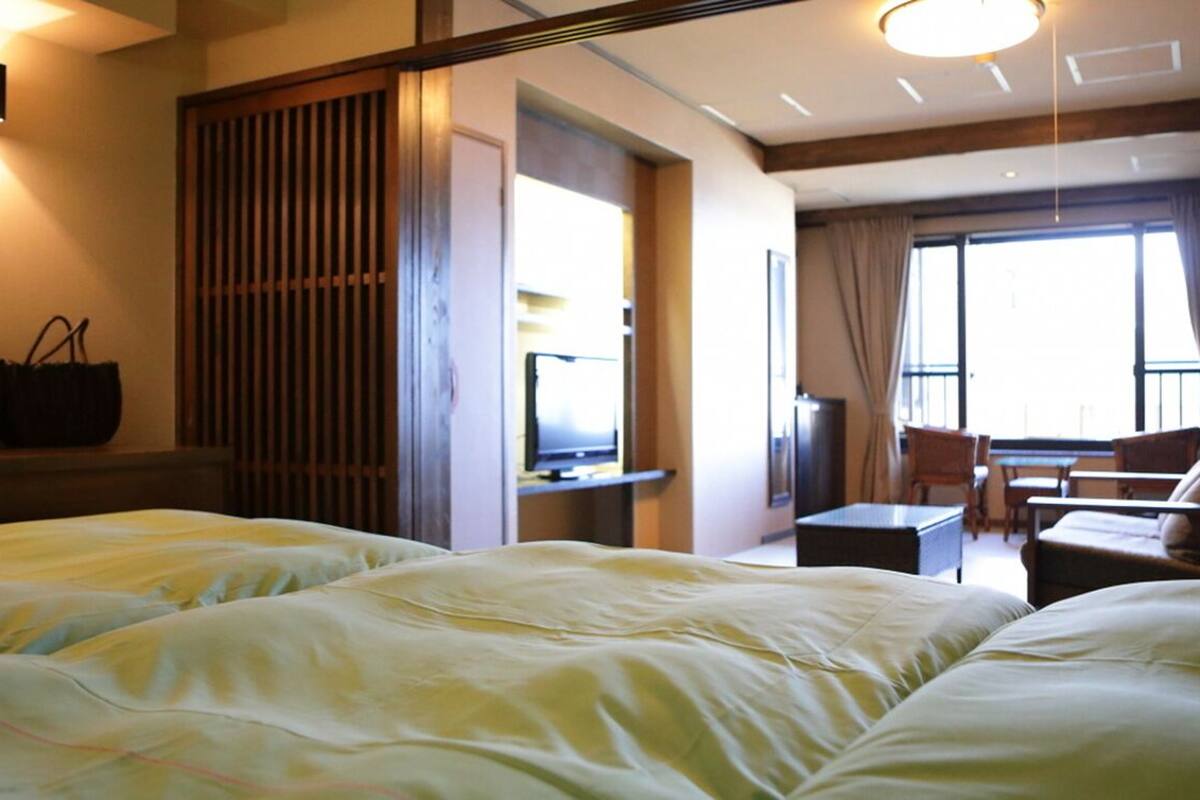 A hotel room with two beds, a desk, a chair, and a balcony with a view.
