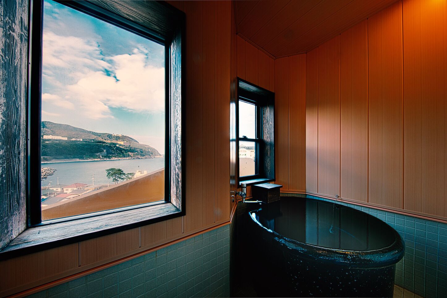 A bathroom with a large window, a bathtub, and wooden paneling.