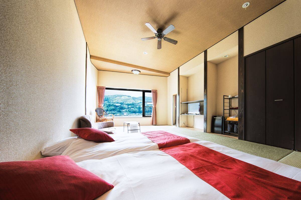 A hotel room with two beds, a ceiling fan, a large window with a view, and a TV.