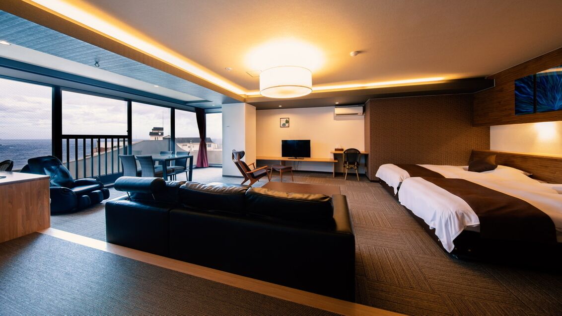 A modern hotel room with a large bed, a sofa, a desk, a TV, and a balcony with a view.
