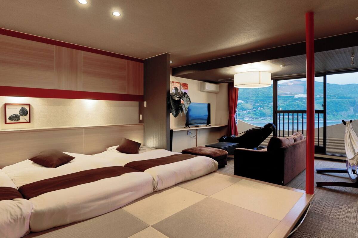 A modern hotel room with a large bed, a desk with a chair, a TV, and a balcony with a view.