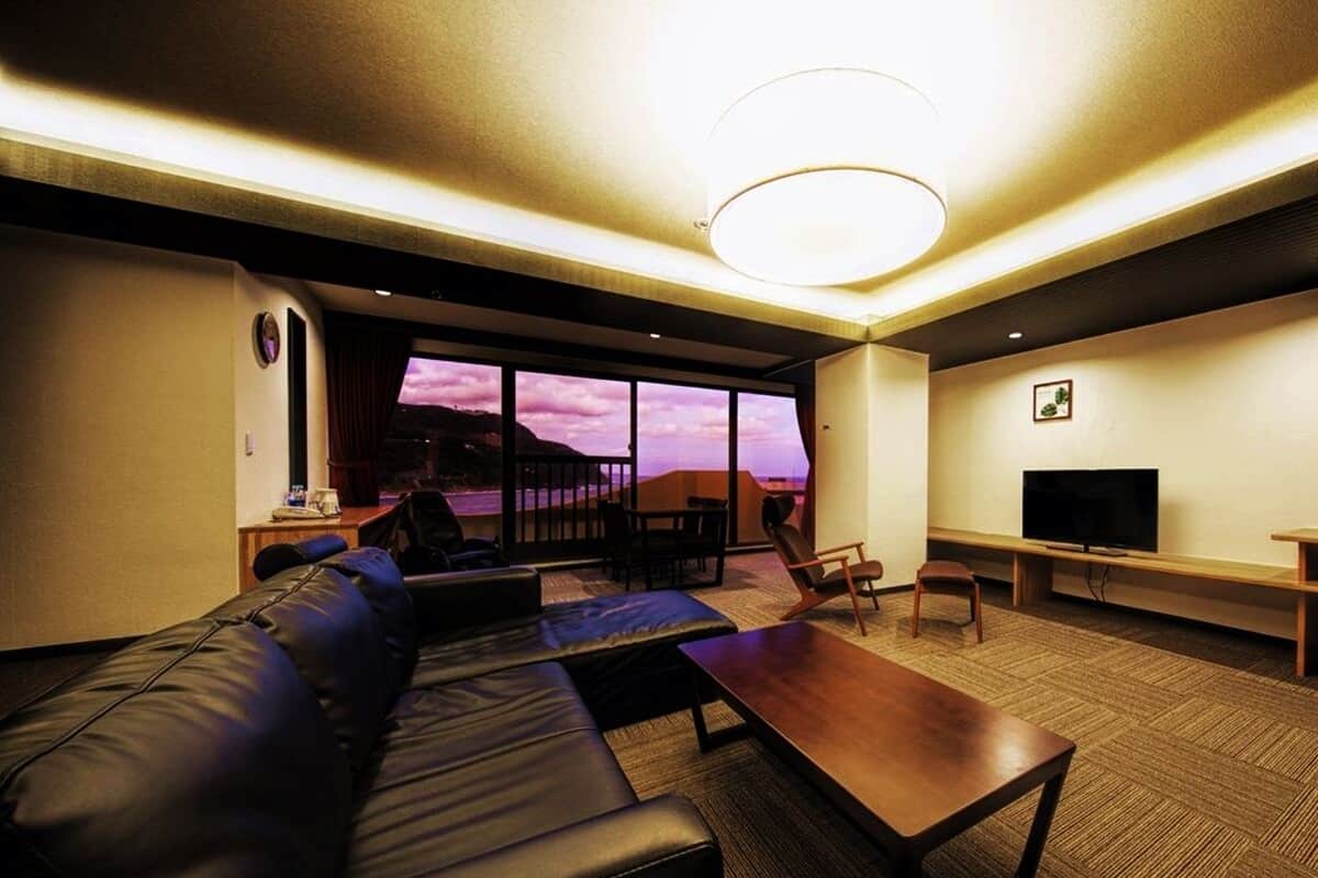 A hotel room with a large sofa, a wooden coffee table, a TV, and a balcony with a view.