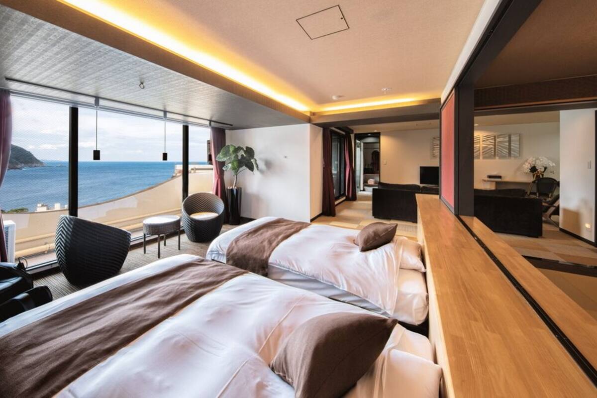 A modern hotel room with two beds, a wooden desk, a view of the sea, and a balcony.