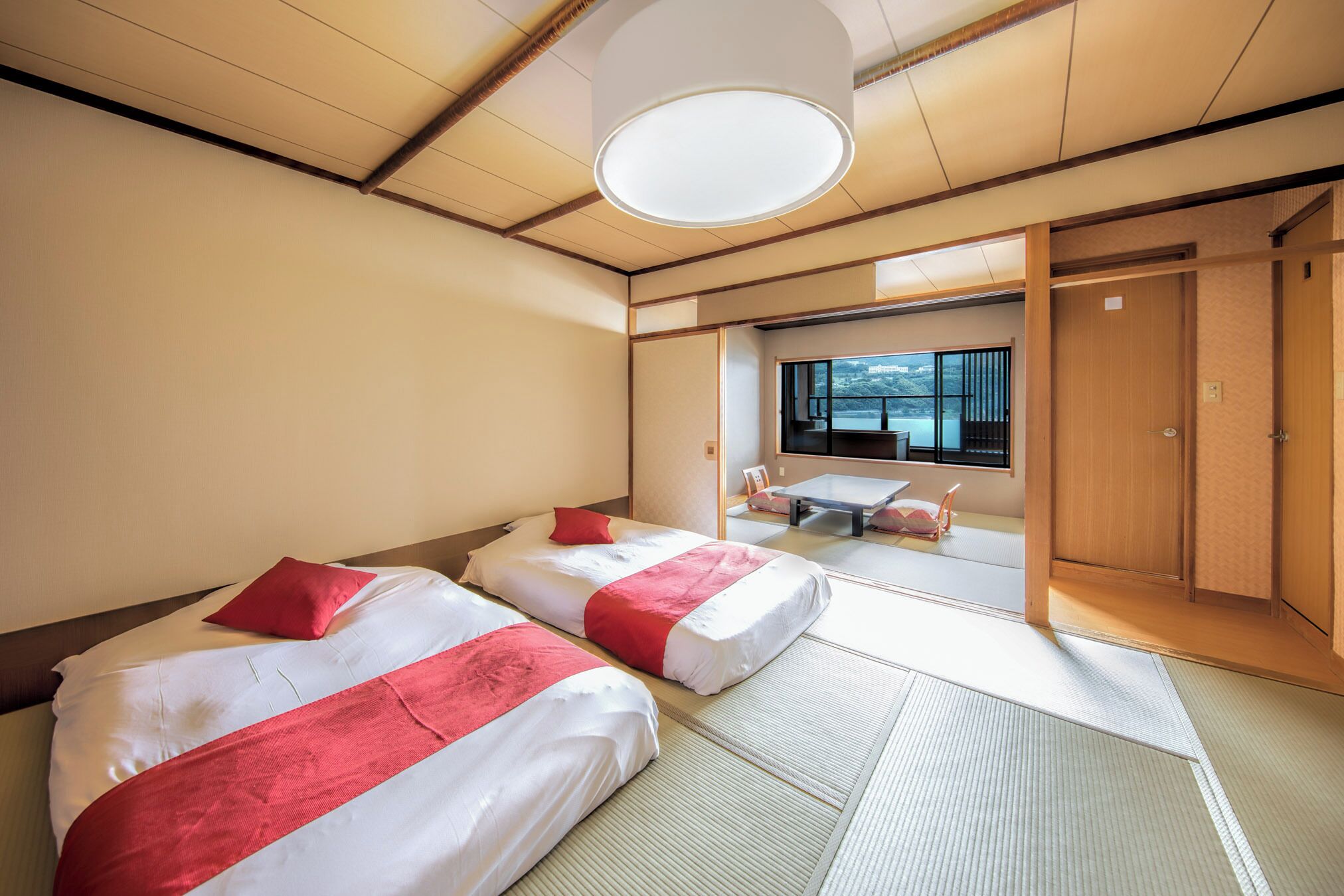 A hotel room with two beds, tatami flooring, a large window with a view, and a traditional Japanese sliding door.
