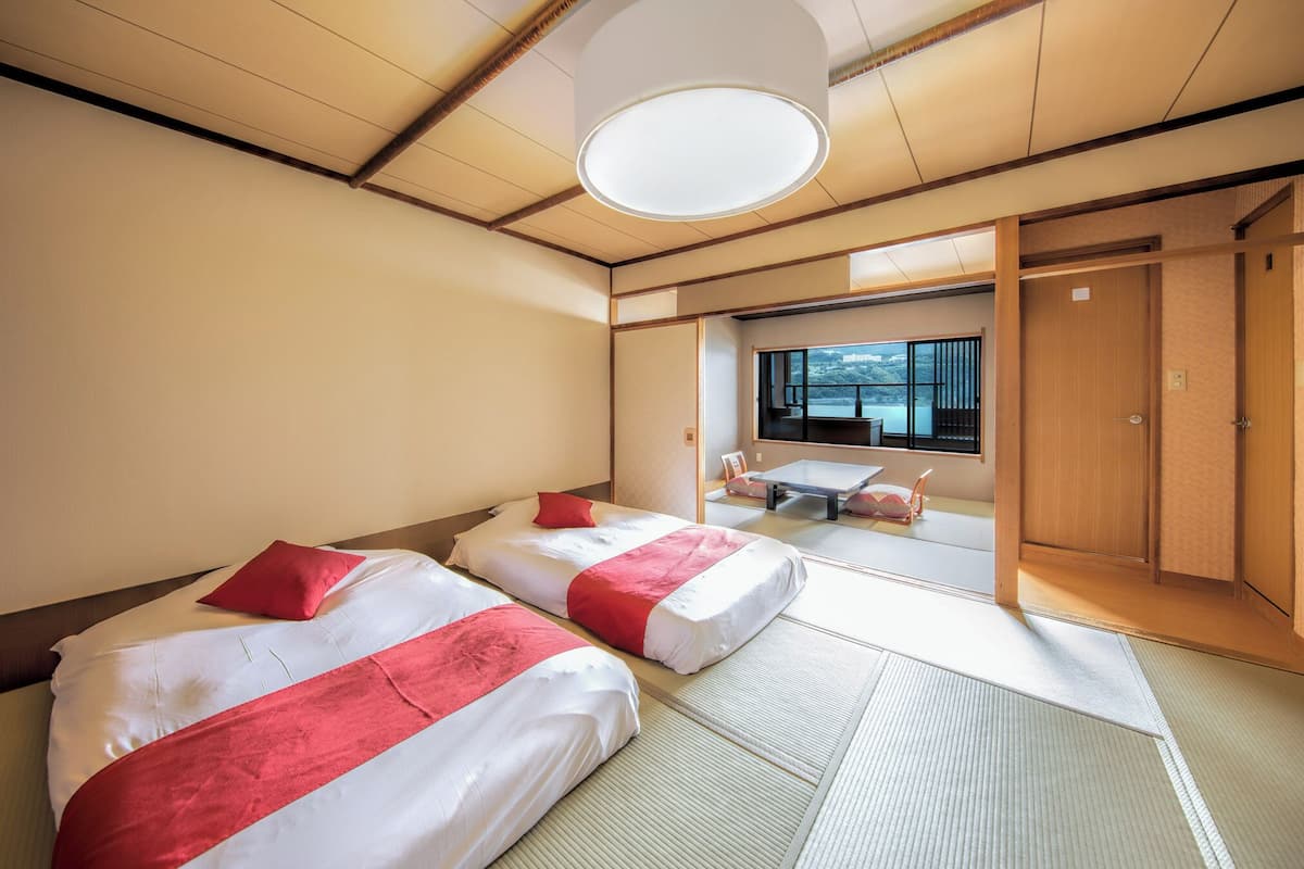A hotel room with two beds, tatami flooring, a large window with a view, and a traditional Japanese sliding door.