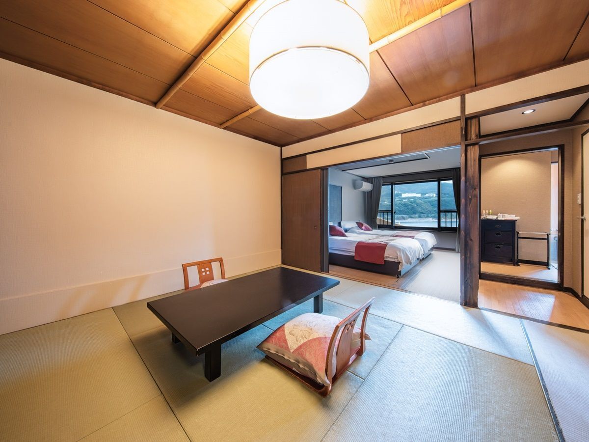 A traditional Japanese-style room with tatami flooring, a low table, and a bed with a view.