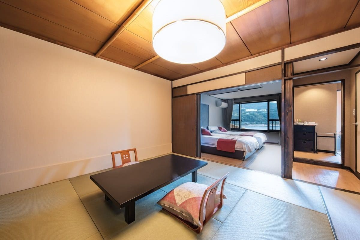 A traditional Japanese-style room with tatami flooring, a low table, and a bed with a view.