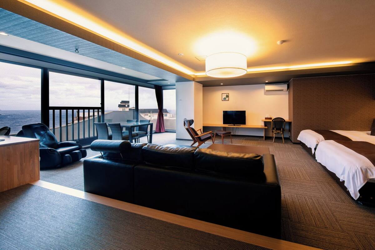 A hotel room with a balcony, a sofa, a desk, a TV, and two beds.