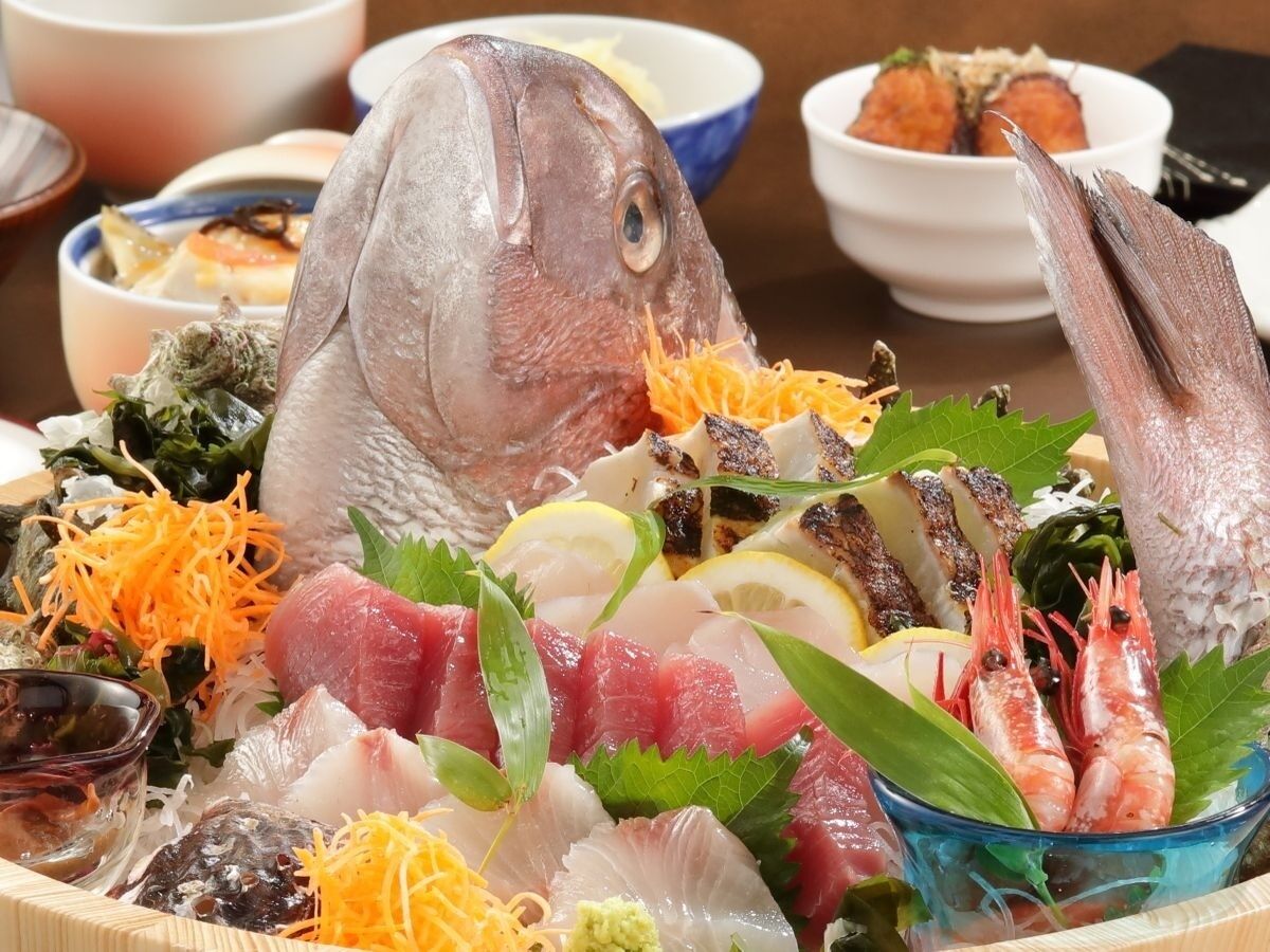 A variety of seafood including fish, shrimp, and possibly sashimi, arranged on a table with a bowl of soup and other dishes in the background.