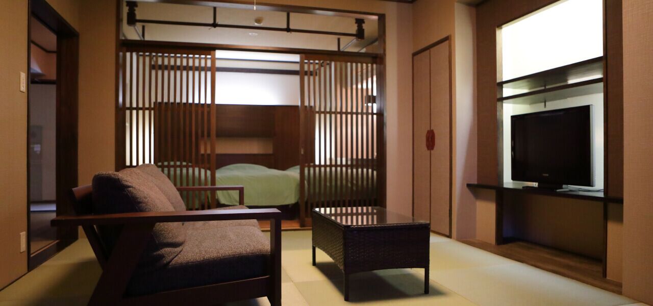 A room with a bed, a chair, a small table, and a TV mounted on the wall.