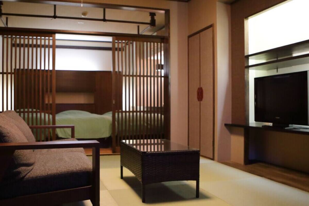 A room with a bed, a chair, a small table, and a TV mounted on the wall.
