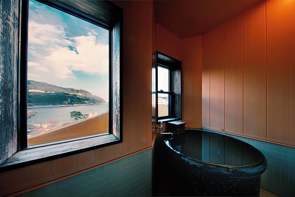 A bathroom with a large window, a bathtub, and wooden walls.