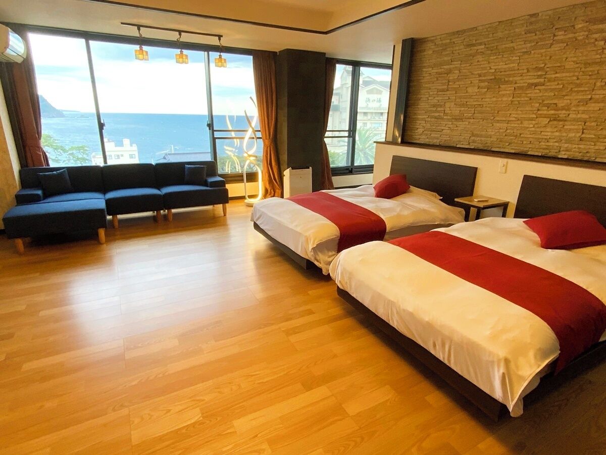 A hotel room with two beds, a sofa, a small table, and a view of the sea.