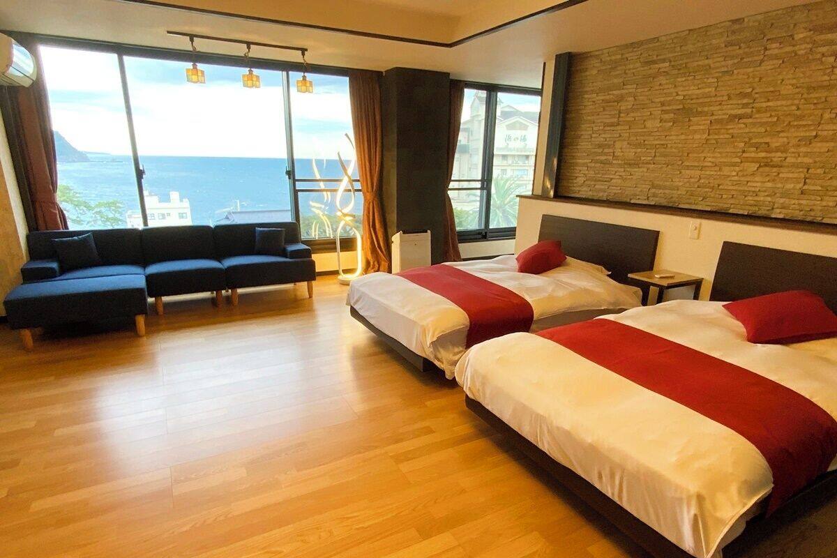 A hotel room with two beds, a sofa, a small table, and a view of the sea.