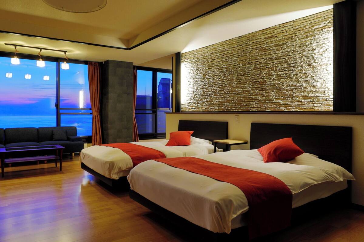 A hotel room with two beds, a sofa, a small table, and a view of the ocean.
