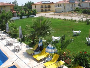 Ein Poolbereich mit Liegestühlen, Sonnenschirmen und einer Rasenfläche.