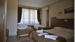 A hotel room with three beds, a wooden headboard, a small table, and a window with curtains.