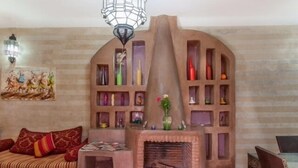 A cozy living room with a fireplace, a sofa with patterned cushions, and a wall-mounted shelf with various decorative items. - Dar Kamar Zamane - Adults Only (Marrakech)