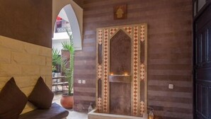 A stone bench with cushions, a tiled fireplace with a geometric pattern, and a potted plant in a courtyard. - Dar Kamar Zamane - Adults Only (Marrakech)
