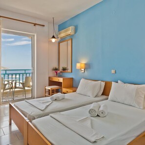 Une chambre d’hôtel avec deux lits, un bureau, une chaise, un balcon avec vue et un ventilateur de plafond.