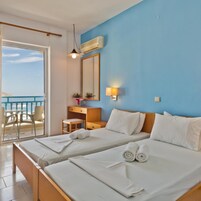 Habitación de hotel con dos camas, un escritorio, una silla, un balcón con vistas y un ventilador de techo.