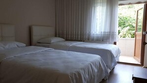 Hotellihuone, jossa on kaksi sänkyä, suuri ikkuna läpikuultavilla verhoilla ja näkymä vehreään maisemaan.