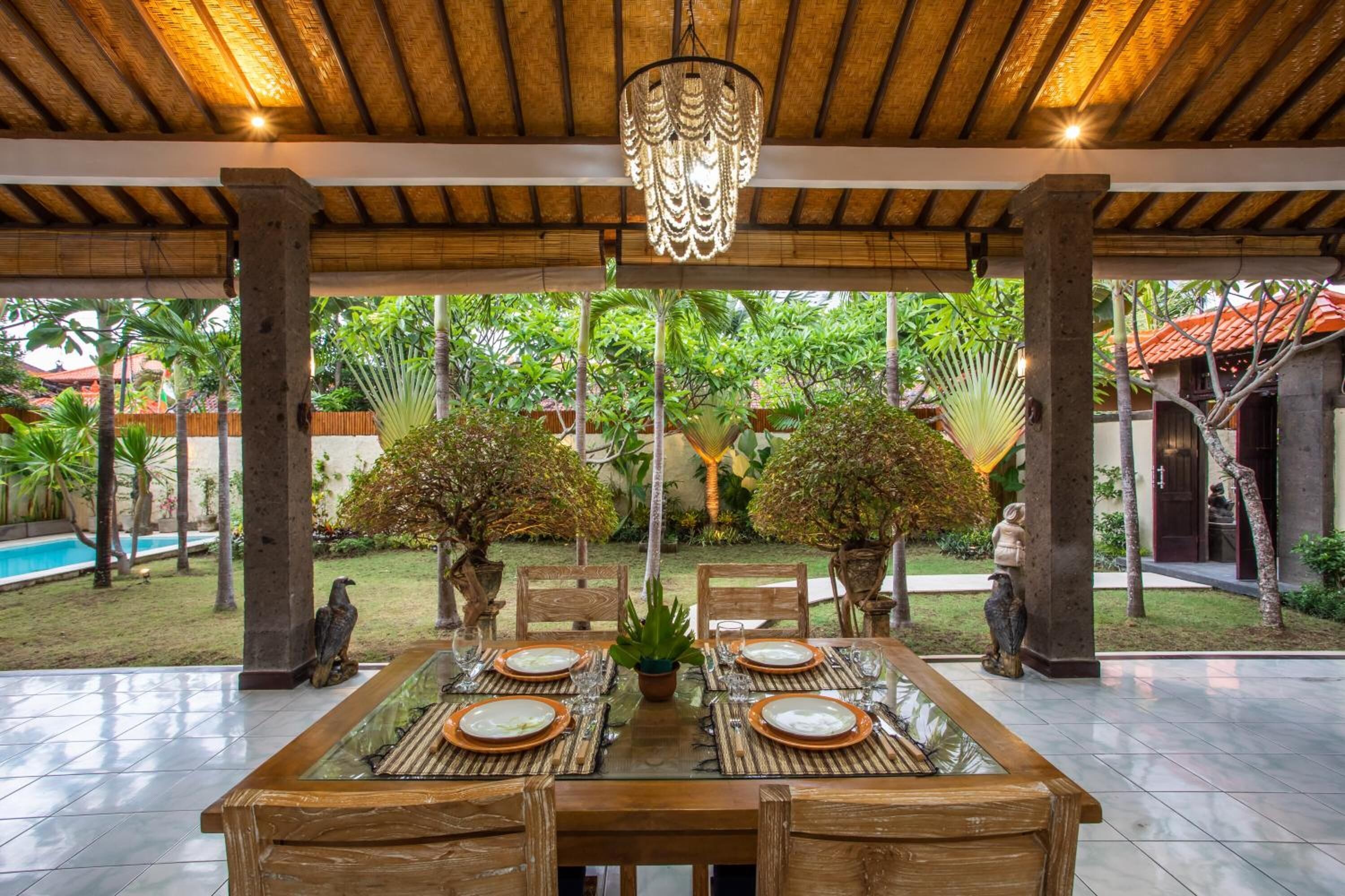 An outdoor dining area with a glass-top table, wooden chairs, and a hanging light fixture.