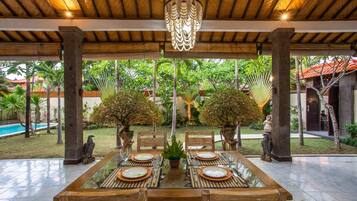 An outdoor dining area with a glass-top table, wooden chairs, and a hanging light fixture.