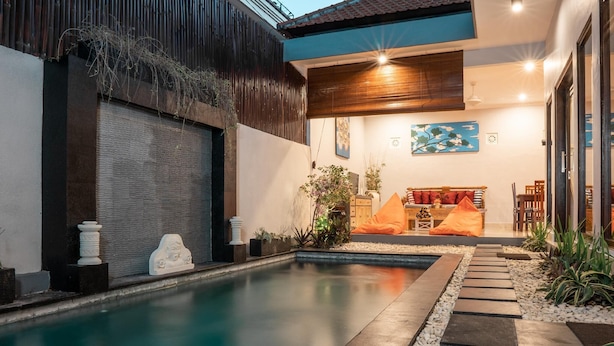 A modern pool area with a clear pool, stone pathway, and a seating area with cushions. - The Catur Villa (Seminyak)