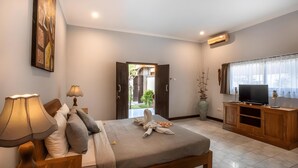 A bedroom with a bed, bedside lamps, a TV, a wooden cabinet, and a painting on the wall. - The Catur Villa (Seminyak)