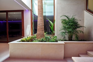 A modern indoor space with a central planter, a staircase, and a glass wall. - Apartamentos Ponent (Calvia)