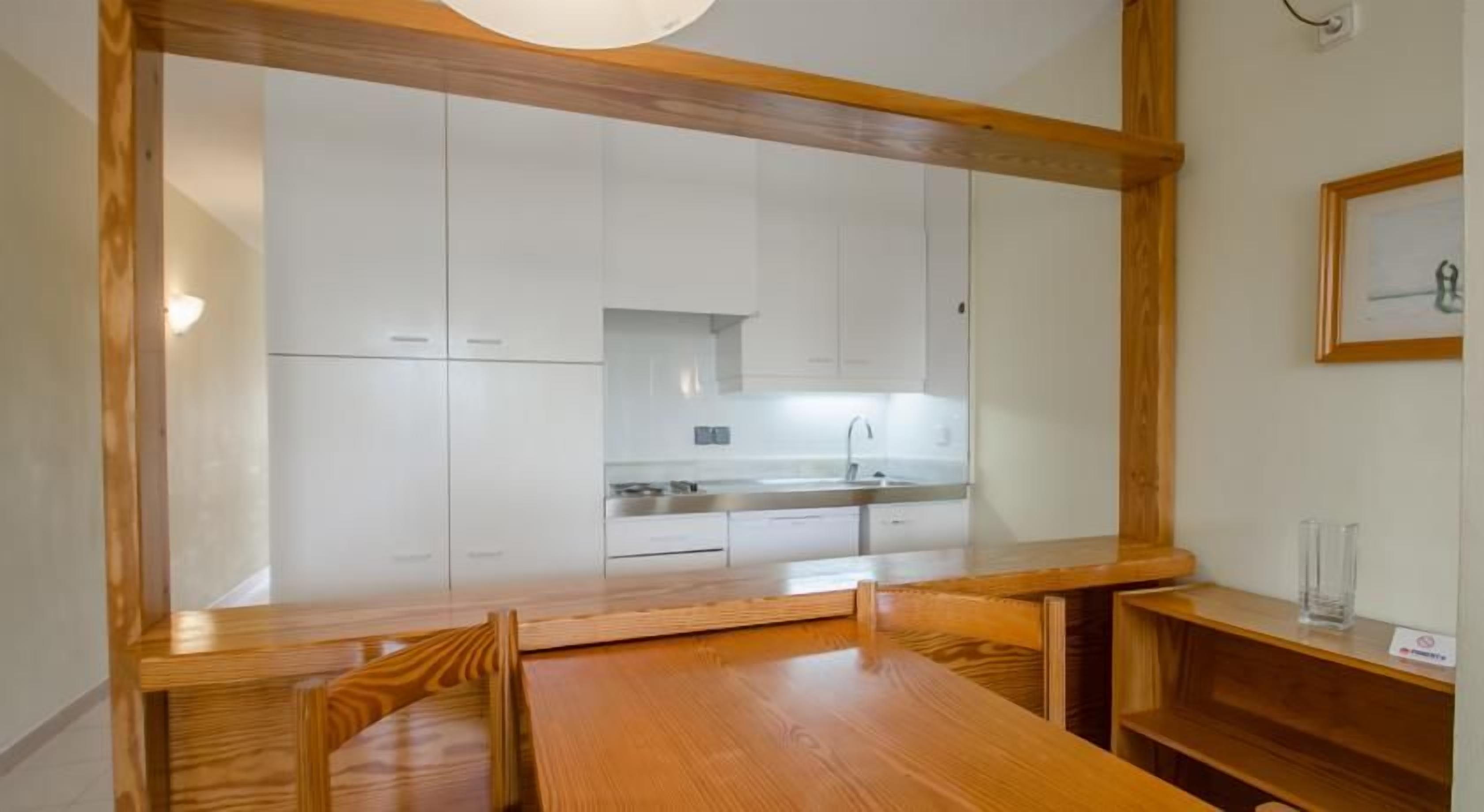 A dining area with a wooden table and chairs, a kitchen in the background, and a framed picture on the wall.