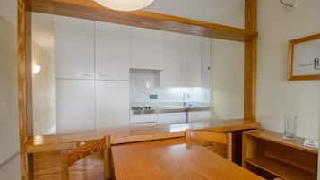 A dining area with a wooden table and chairs, a kitchen in the background, and a framed picture on the wall.
