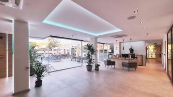 Un hall d’entrée spacieux au design moderne, comprenant un comptoir d’accueil, un espace salon et de grandes fenêtres donnant sur la terrasse extérieure.