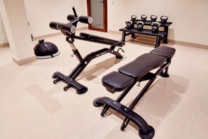 Un gimnasio con equipo de ejercicio, incluyendo una banca, mancuernas y una pesa rusa.