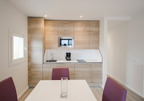 A modern kitchen with a built-in microwave, a coffee maker, and a sink. There is a dining table with chairs in front. - Apartamentos Ponent (Calvia)