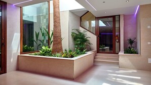 A modern interior with a glass wall, a wooden staircase, and a planter with plants. - Apartamentos Ponent (Calvia)