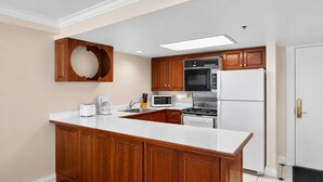 Cocina con armarios de madera, encimera blanca, horno empotrado, microondas y refrigerador.