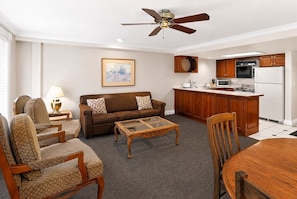 A living room with a sofa, chairs, a coffee table, a ceiling fan, and a kitchen area with a refrigerator, microwave, and cabinets. - Park Hotel Condominiums (Park City)